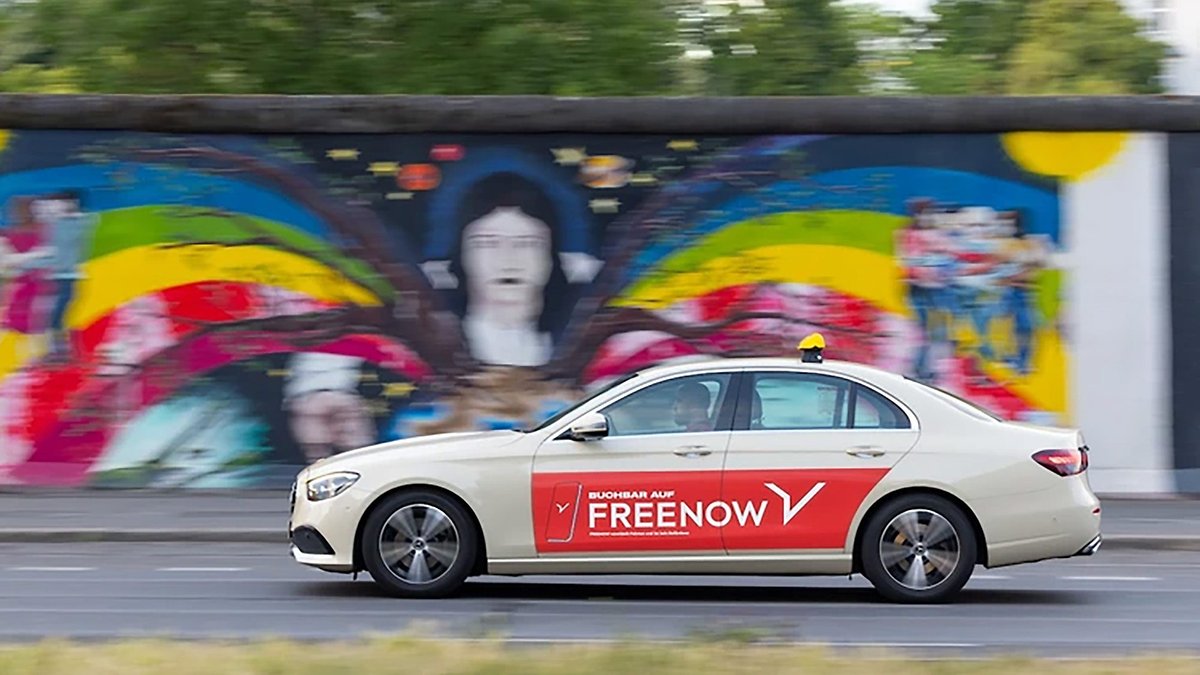 A beige car with a red 'FREENOW' logo drives past a colorful mural.