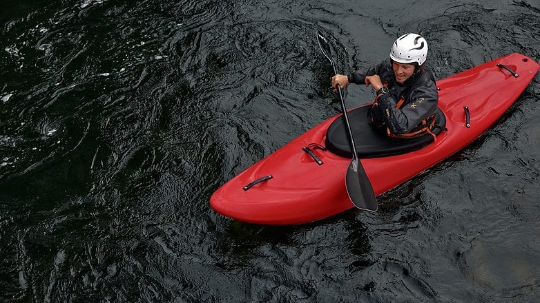 A person paddling a red kayak on dark water, wearing a helmet and a wetsuit. A person paddling a red kayak on dark water, wearing a helmet and a wetsuit.