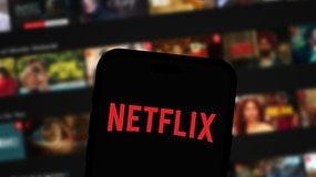 Netflix logo on smartphone screen, Netflix home screen in the background.