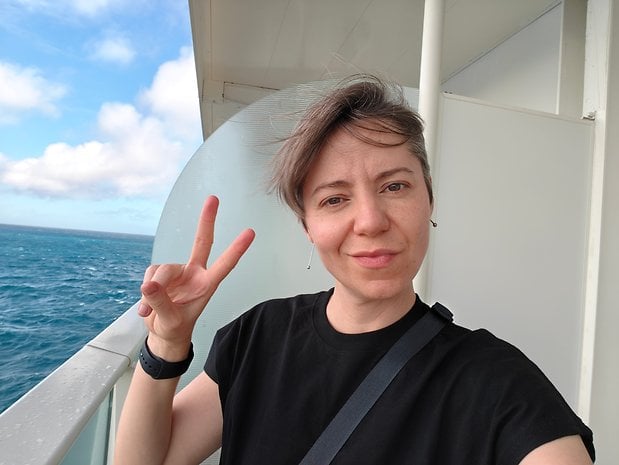 A person making a peace sign on a balcony with ocean views in the background.