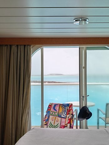 A colorful chair by a large window with a view of a turquoise sea and distant island.