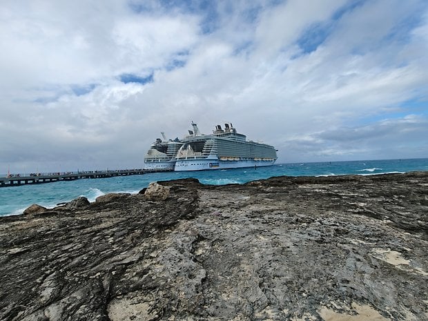 A large cruise ship docked near rocky shore under cloudy skies.