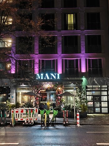 Vista noturna de um restaurante com iluminação colorida e bicicletas e patinetes estacionados.