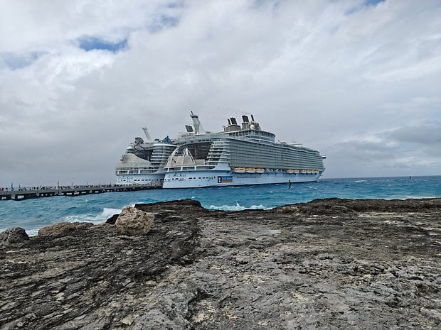 A large cruise ship docked near rocky shores with a cloudy sky overhead.