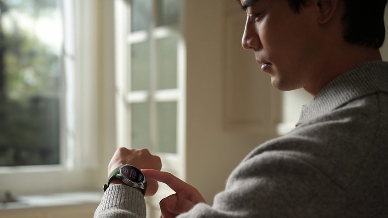 A person wearing a OnePlus Watch 3 and checking the screen while standing by a window.