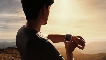 A person checking their OnePlus Watch 3 while enjoying a scenic view at sunset.