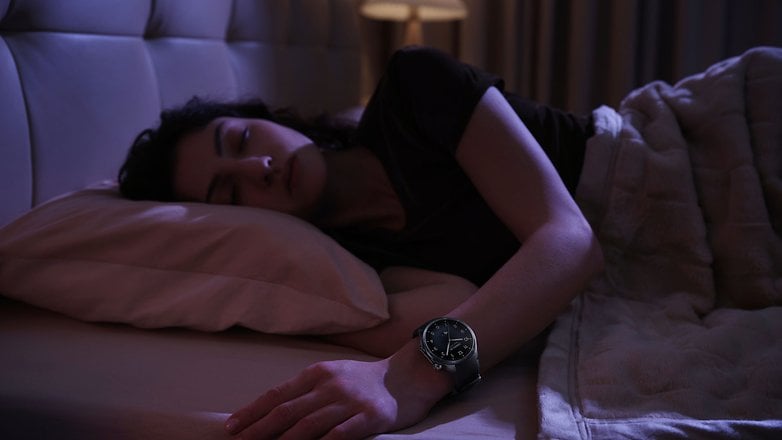 A person sleeping on a bed, wearing a OnePlus Watch 3 on their wrist.