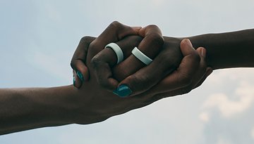 Two hands clasped together, wearing Oura Rings, against a cloudy sky.