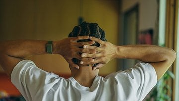 A person with braided hair, wearing a Polar Loop, rests hands behind their head in a relaxed pose.