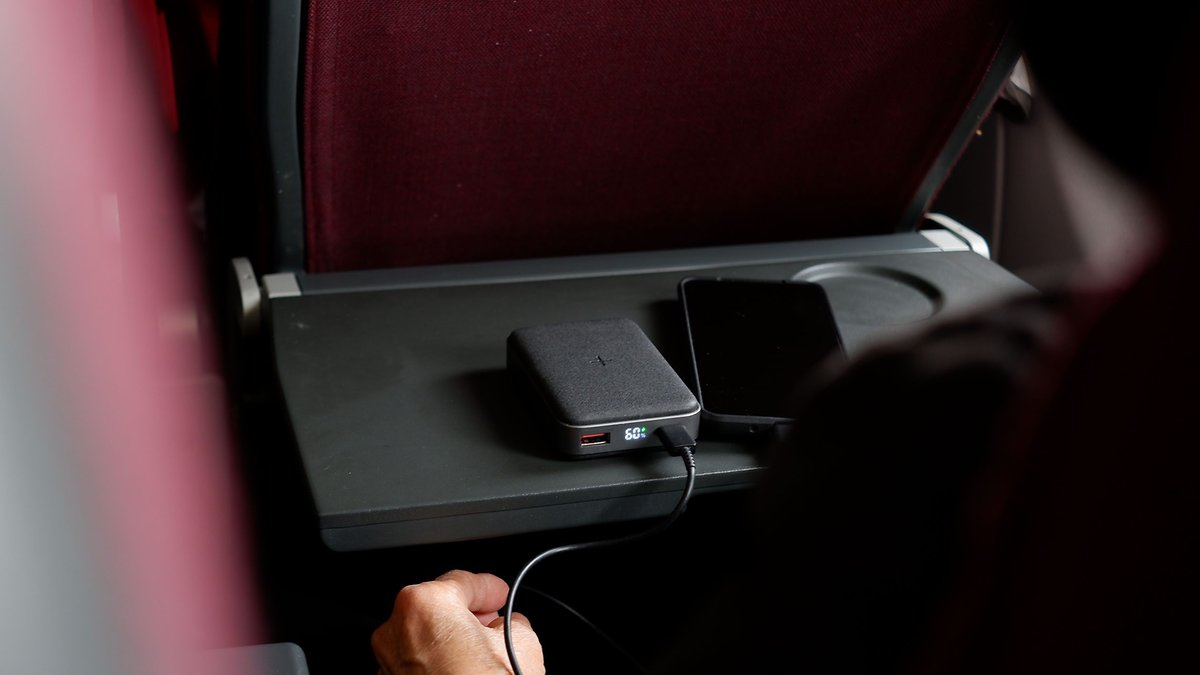 A power bank connected to a smartphone on a tray table in an airplane.