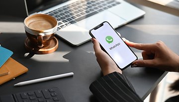 A person holding an iPhone with the WhatsApp logo in the home screen