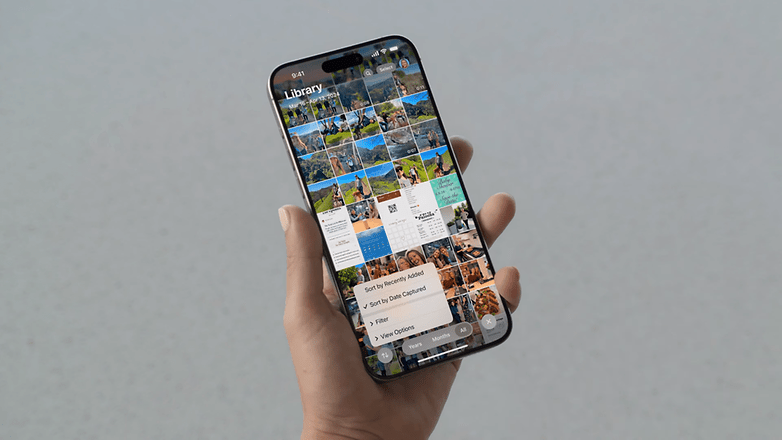 Un iPhone vu de face et tenu dans une main gauche avec son écran allumé affichant l'application photo d'iOS 18.