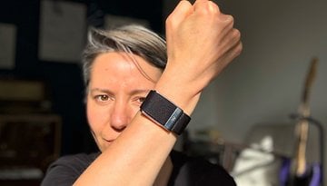 A person shows a Whoop MG fitness tracker on their wrist, smiling at the camera.