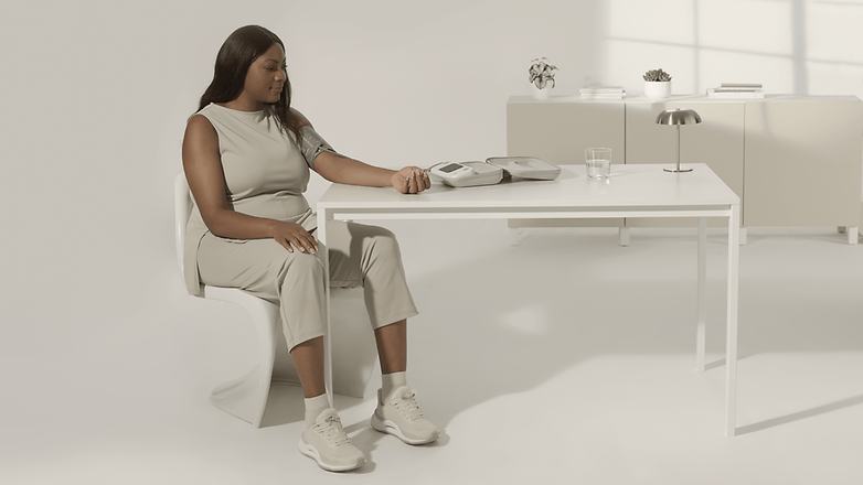 A woman sitting at a table, measuring her blood pressure with a device.