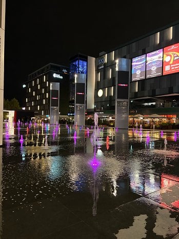 Night view of a plaza with colorful fountains and modern buildings.
