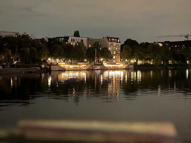Nighttime view of a waterfront with illuminated buildings and reflections on the water.