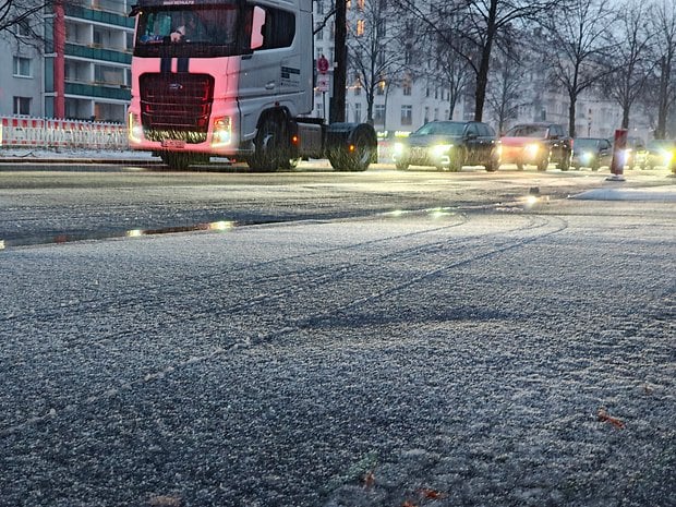 A truck parked on a wet road with tire tracks and blurred traffic in the background during a rainy evening.