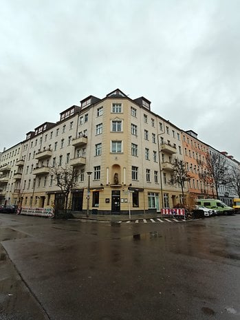 A corner building with balconies on a rainy day, surrounded by a wet street and overcast sky.