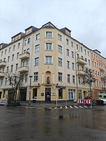 A corner building with multiple windows, featuring a statue above the entrance on a rainy day.