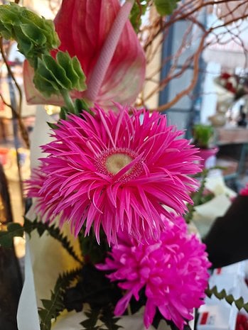 A close-up of vibrant pink flowers with spiky petals and green leaves in a decorative arrangement.