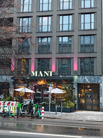 A restaurant named MANT, with outdoor seating, flowers, and e-bikes parked outside, on a rainy day.