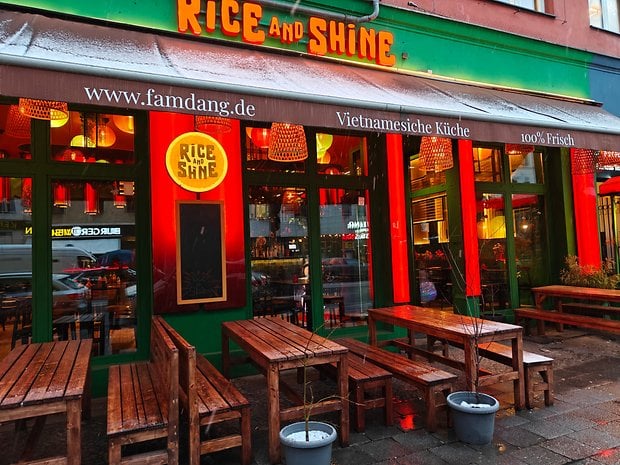 The exterior of Rice and Shine, a Vietnamese restaurant with wooden tables and colorful lanterns.