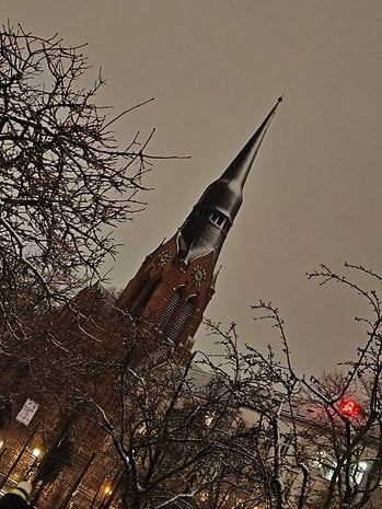 A church steeple rising above bare branches, under a gray sky, with a hint of snow.