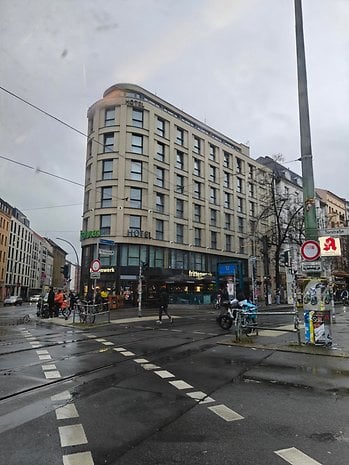 A hotel building at an intersection with traffic lights and pedestrians on a rainy day.