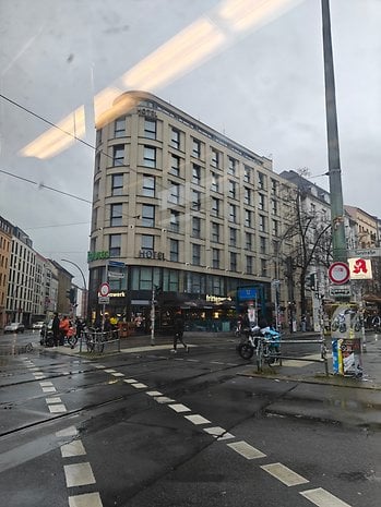 A street view featuring a hotel building, bicycles, and people crossing on a rainy day.