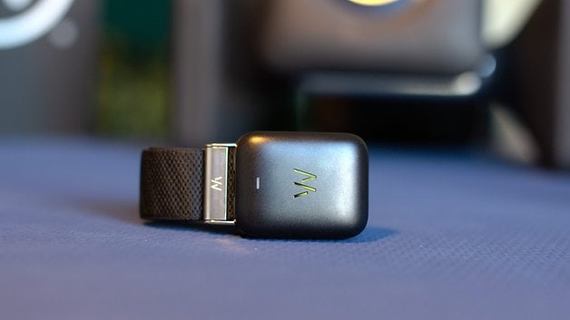 A Whoop MG sensor device lying on a blue surface with a black strap.