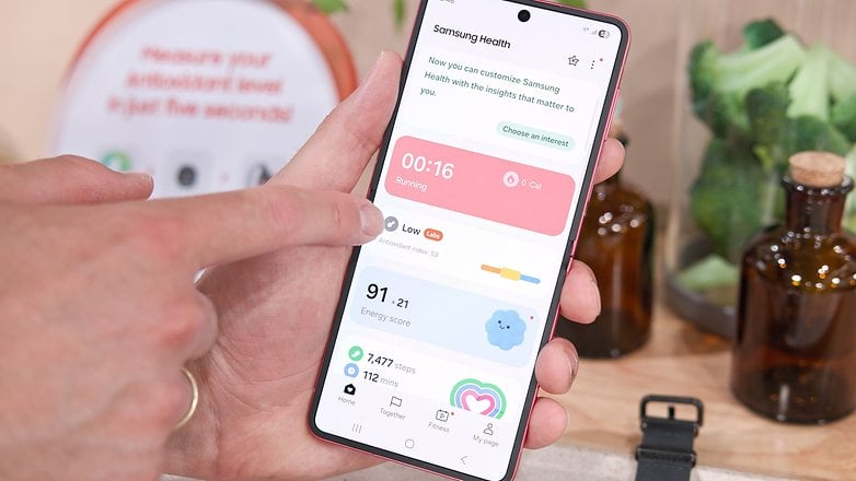 A person interacting with the Samsung Health app on a smartphone, displaying running stats and antioxidant level.