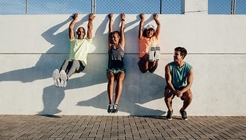 Four individuals exercising on a wall, smiling and engaged in fitness activities.