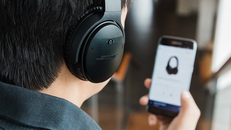 A Bose headphone highlighted with smartphone screen blurred in the background.