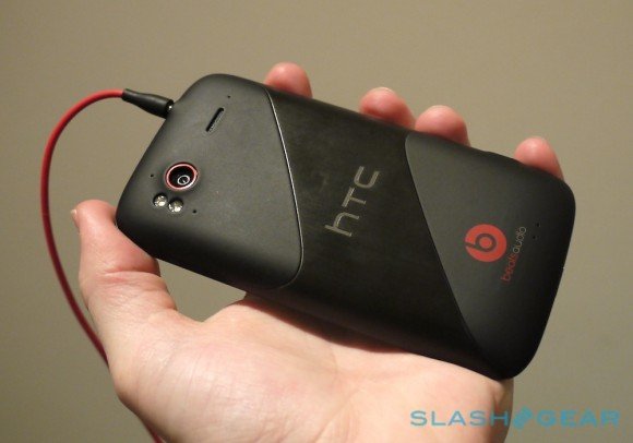 Un smartphone HTC noir avec des écouteurs rouges, tenu dans une main, montrant le logo Beats Audio au dos.