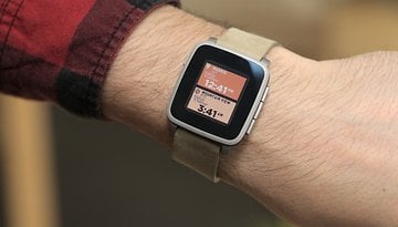 A wrist wearing a Pebble Time smartwatch displaying time and location.
