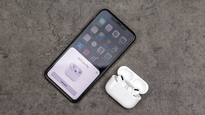 Apple AirPods Pro dengan sarung pengecas di sebelah iPhone di atas meja