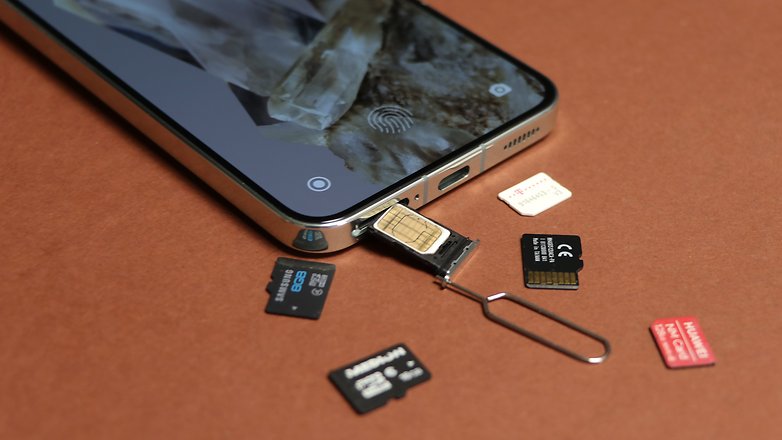 Um cartão SIM inserido em um smartphone, cercado por vários cartões de memória em um fundo marrom.