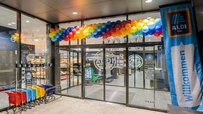 Eingang eines ALDI-Marktes, dekoriert mit bunten Ballons und einem Banner mit der Aufschrift 'Willkommen'.