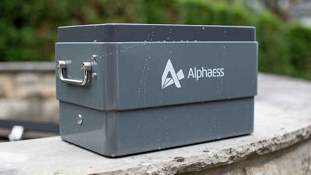 Graue AlphaESS-Batteriespeichereinheit mit Griff, auf einer Steinoberfläche platziert.