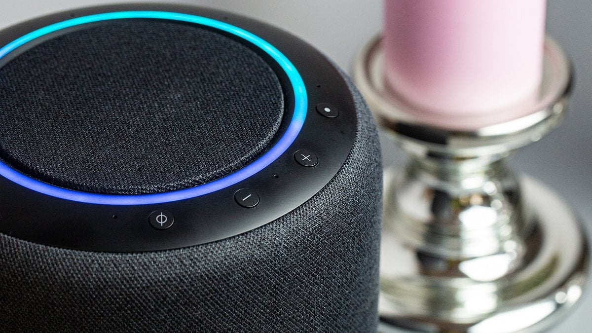 Close-up of a smart speaker with blue ring light and controls, next to a pink candle.