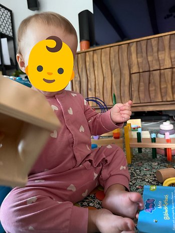 A baby in a pink overall plays with toys on a patterned mat.