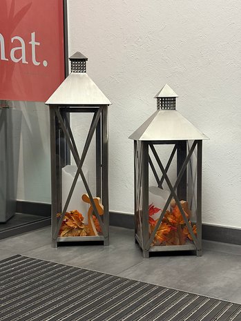 Deux lanternes décoratives avec des feuilles d'automne à l'intérieur, à côté d'un panneau rouge qui dit 'Quoi.'.