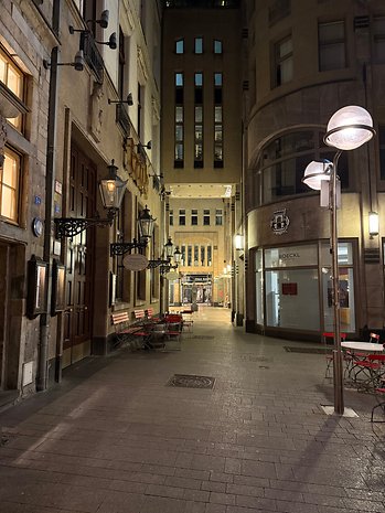 A narrow alley at night with illuminated street lamps, empty chairs, and historic buildings.