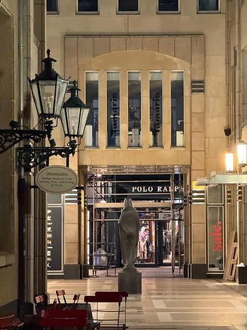 Night view of a shopping arcade with lanterns, a sculpture and the entrance to a store.