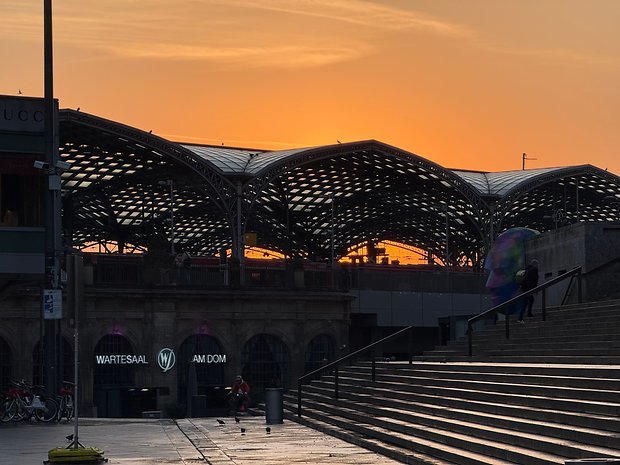 Sonnenuntergang hinter einem modernen Gebäude mit einzigartiger Architektur und einer Person mit einem Regenschirm.