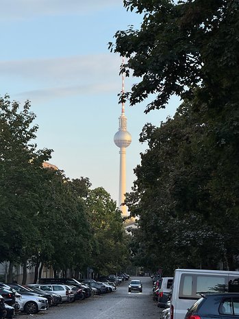 A view of the Berlin TV tower peeking through trees along a street.