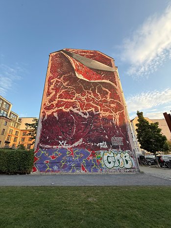 Um grande mural de carne vermelha com uma faca, cercado por grafites coloridos em um prédio.