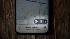 Application Google Maps affichant une limite de vitesse de 20 km/h et une vitesse de 0 km/h sur une surface en bois.