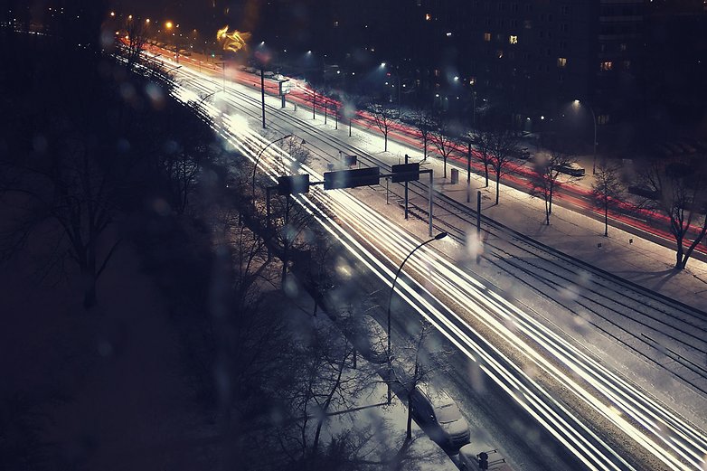 Night view of a snowy street with blurred light trails from moving cars.