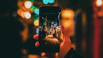 Eine Hand hält ein Smartphone, das eine hell erleuchtete Gasse zeigt.